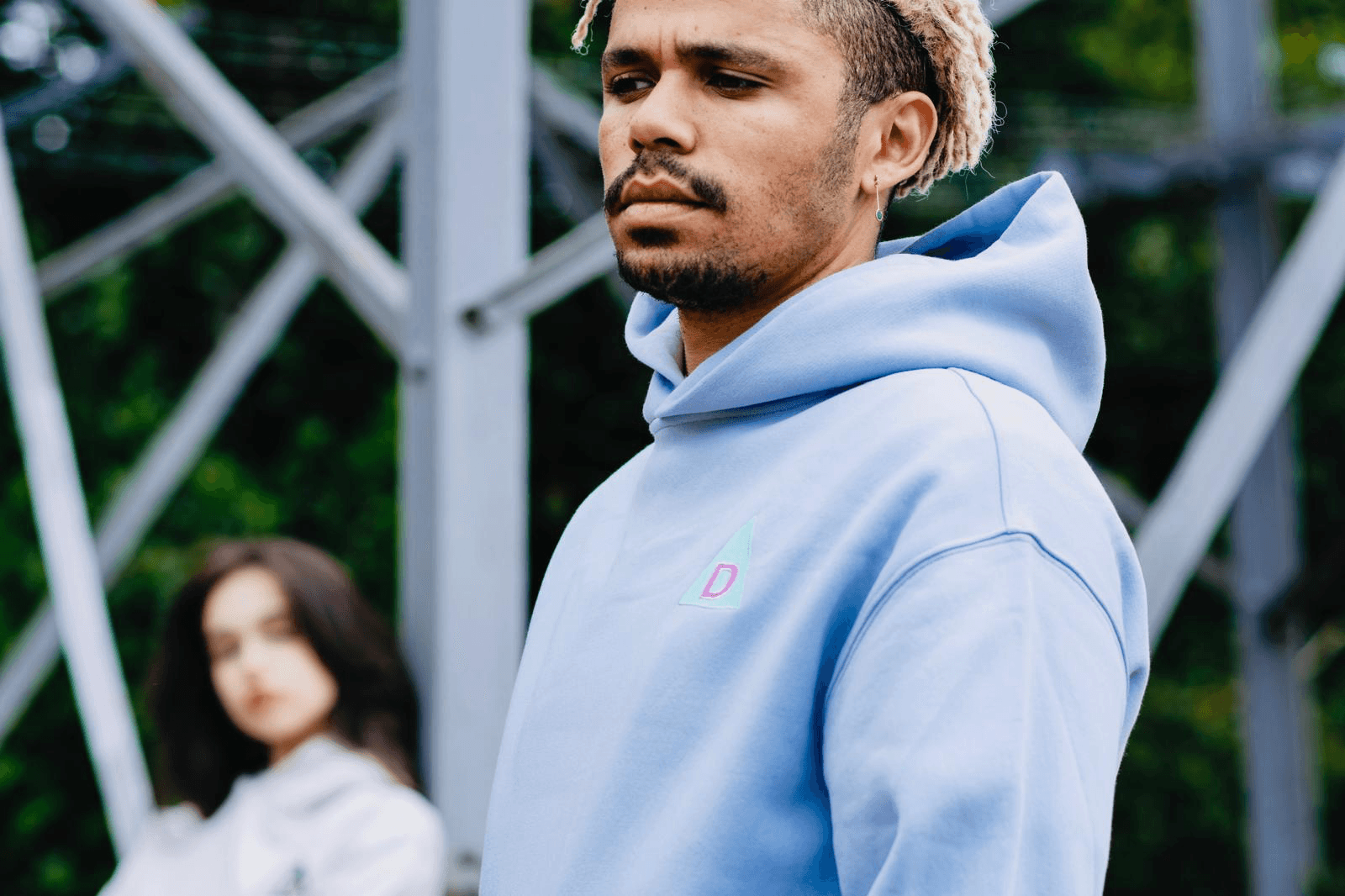 Man wearing The Decried blue hoodie with woman out of focus in background