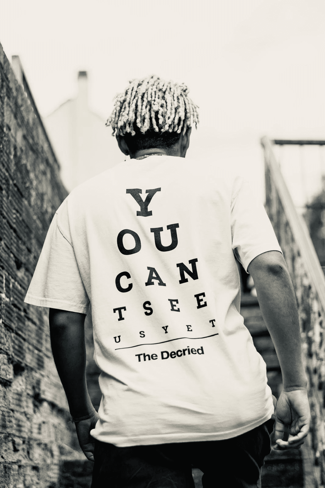 Back view of man wearing The Decried beige tee